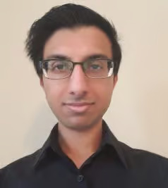 The image shows a man with glasses wearing a black shirt, standing against a plain background.