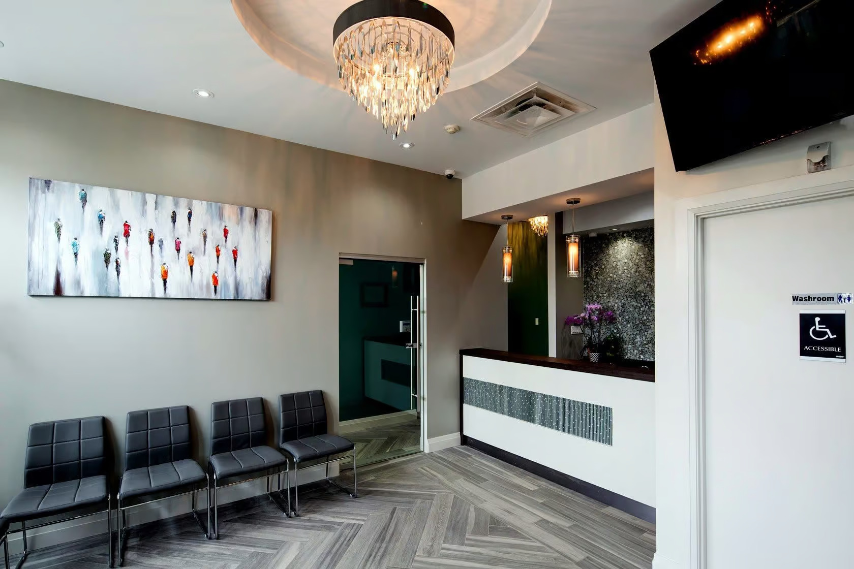 This image depicts a modern interior space with a reception area, featuring a chandelier, decorative wall art, and a waiting area with seating.