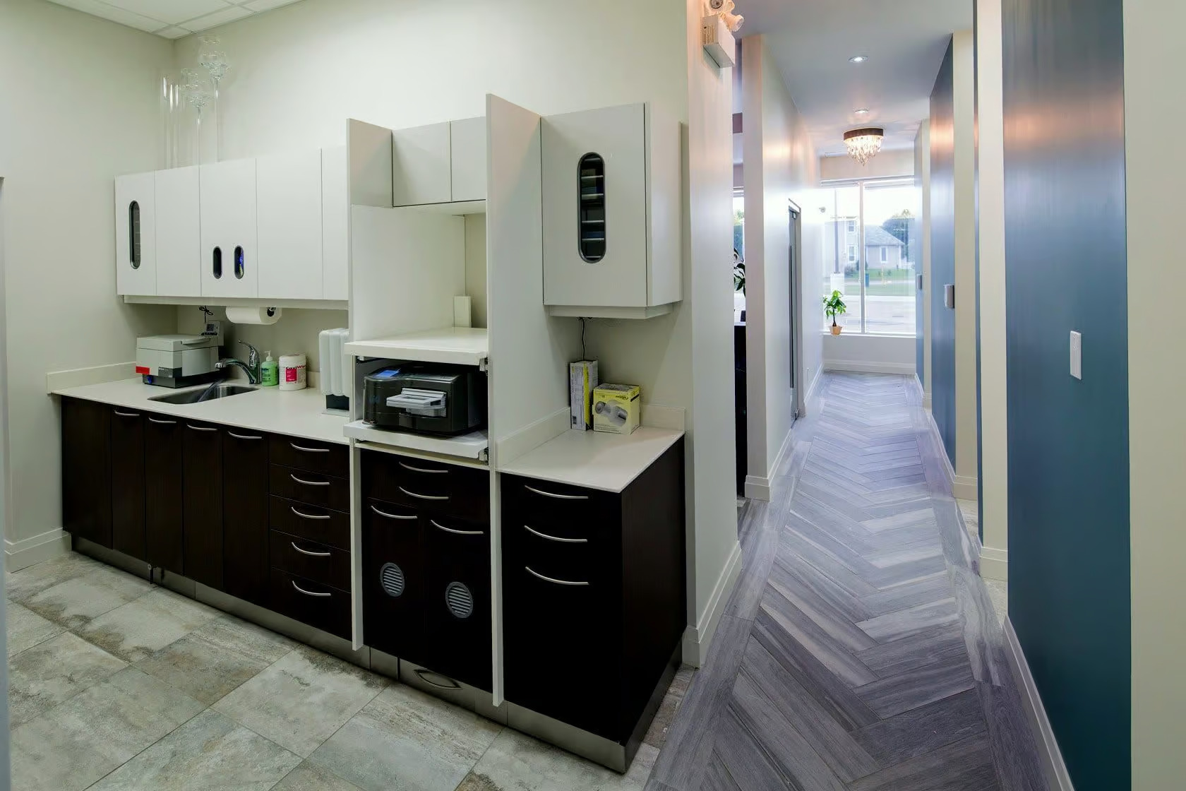 The image shows a modern kitchen with dark cabinets, stainless steel appliances, a white countertop, and a tiled floor.