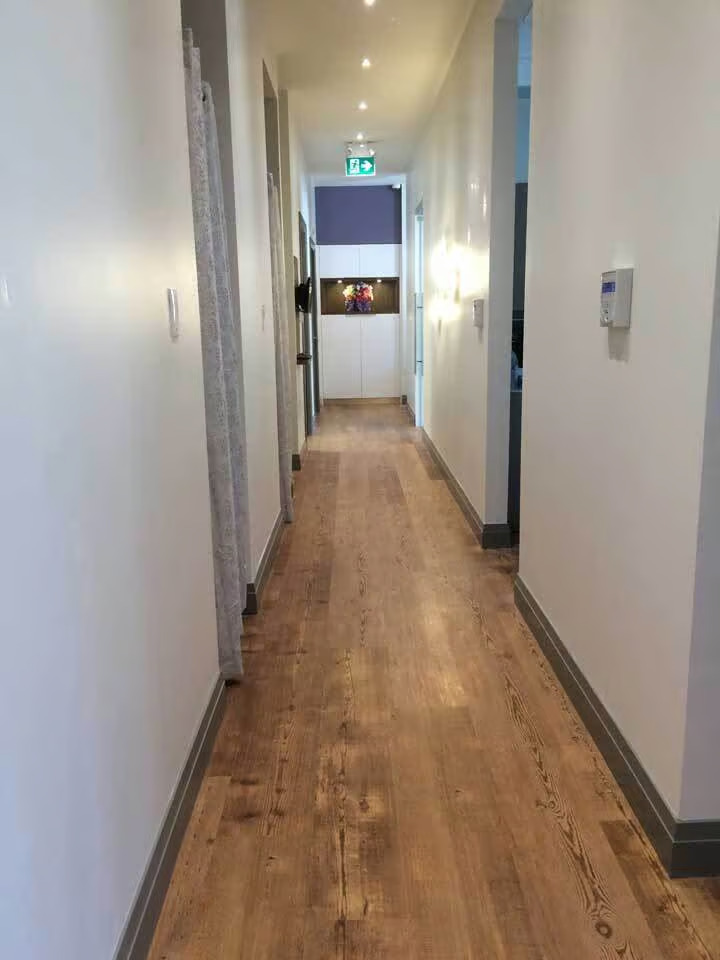 The image shows a long hallway with a wood floor, walls painted white, and doors on either side.