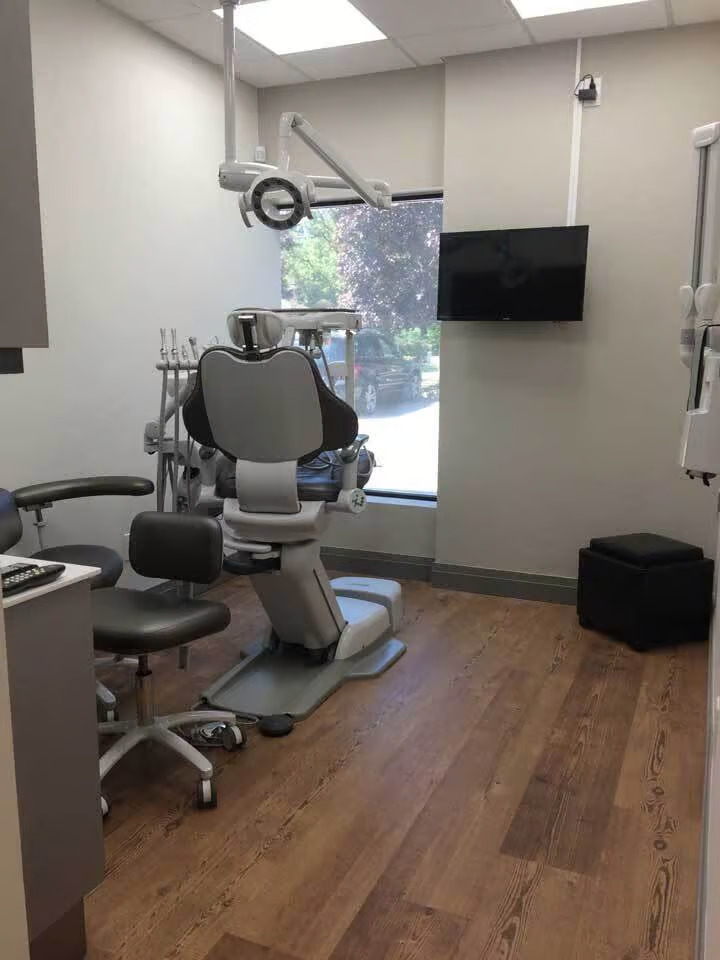 The image shows an interior view of a dental office with a dental chair, equipment, and a waiting area.