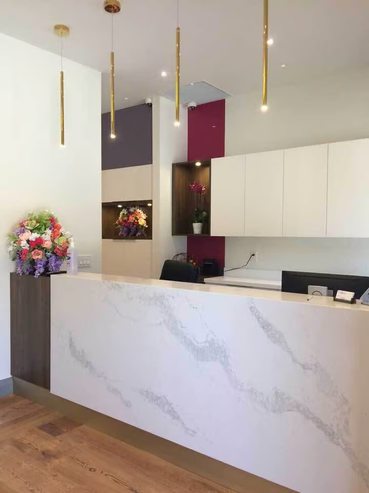 The image shows an interior space featuring a modern reception desk with a marble countertop and a sleek design, set against a backdrop of a clean and minimalist office environment with white walls and a colorful accent wall in the background.
